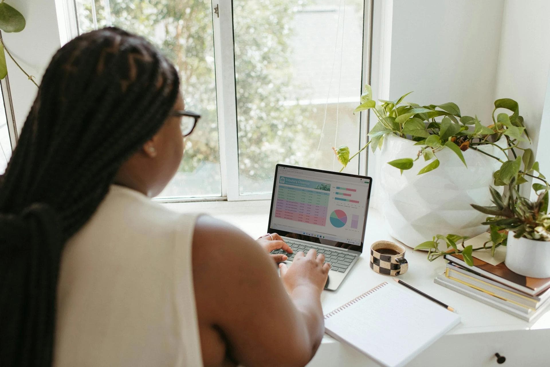 Black woman working at desk on laptop with graphs on screen